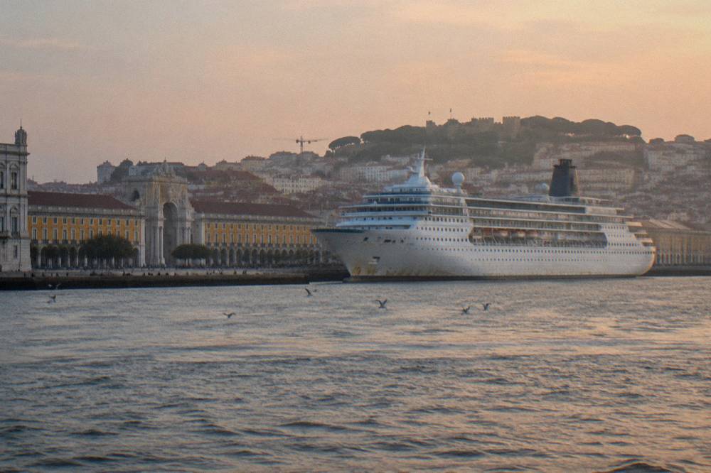 A cruise ship moored on the Tagus river with Lisbon's hillsides and a bridge in the background