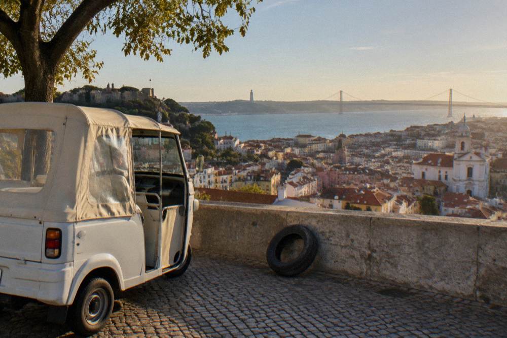 A tuk tuk parked at a viewing terrace overlooking red rooftops and the Tagus river