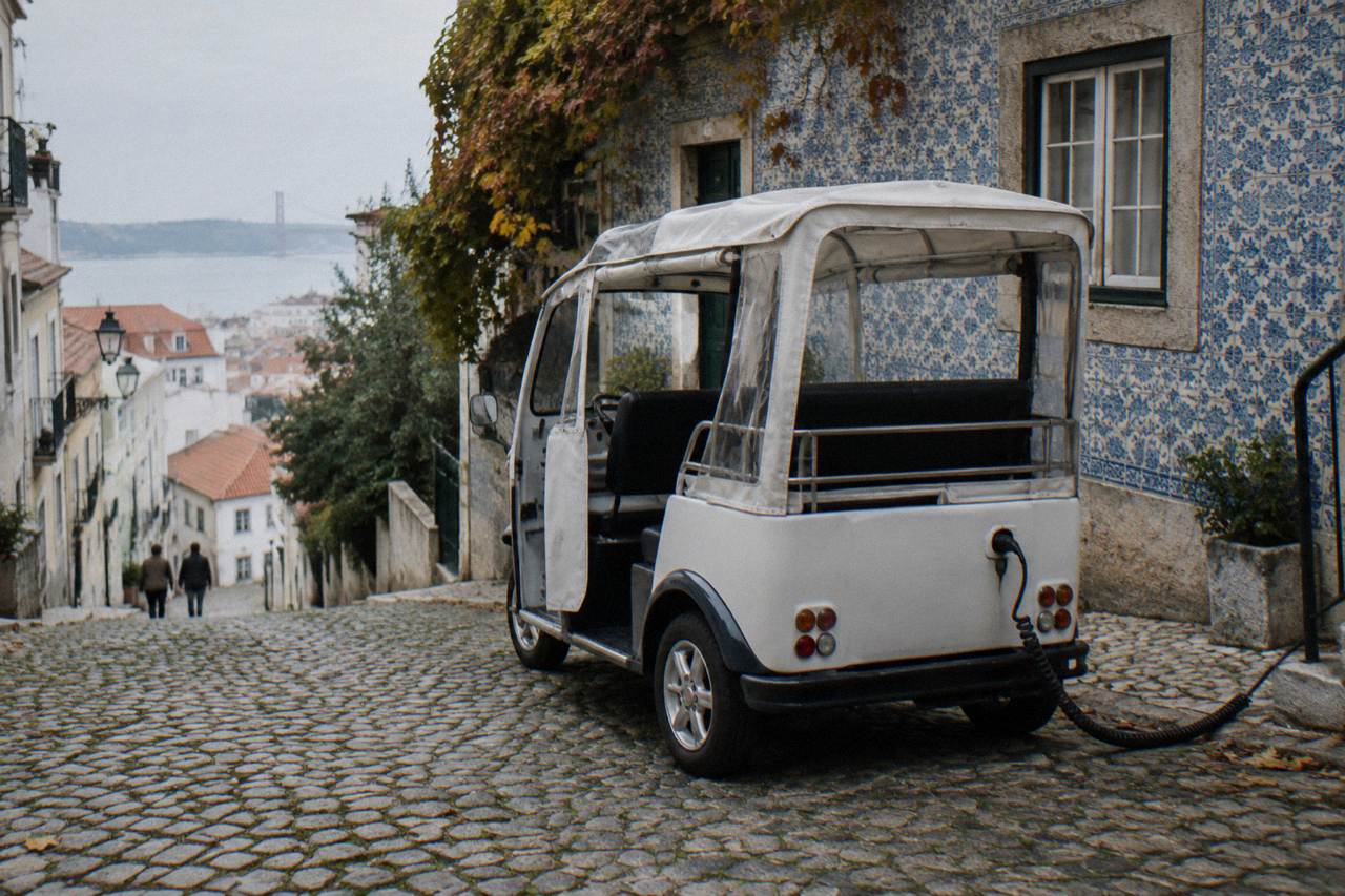A small electric tuk tuk parked on a cobbled Lisbon street beside tiled building facades
