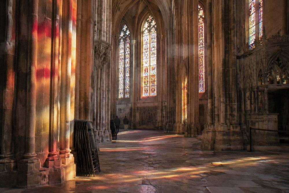 The ornate interior of the Batalha Monastery with tall stone columns and stained glass windows