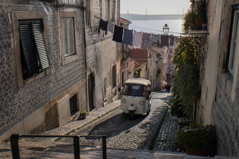 An electric tuk tuk driving up a narrow cobbled street in Alfama with laundry hanging above