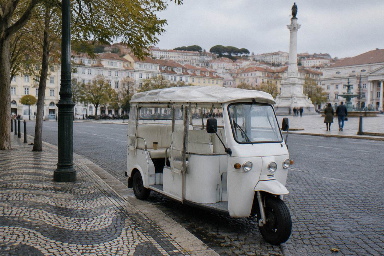 A small electric tuk tuk parked on a cobbled Lisbon street lined with pastel buildings