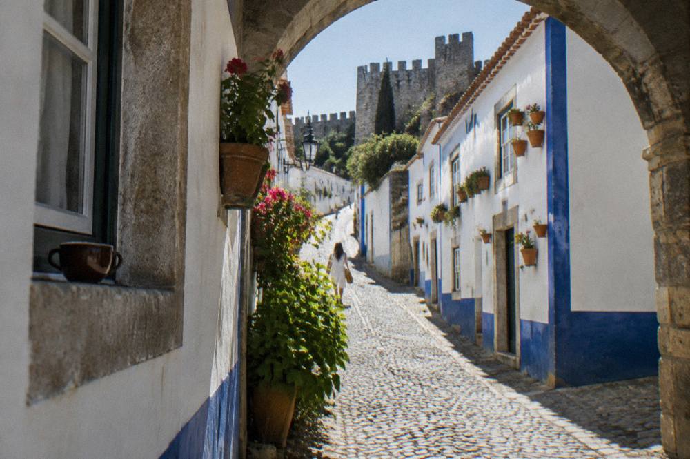 Narrow cobbled street lined with white houses and blue trim leading toward a castle
