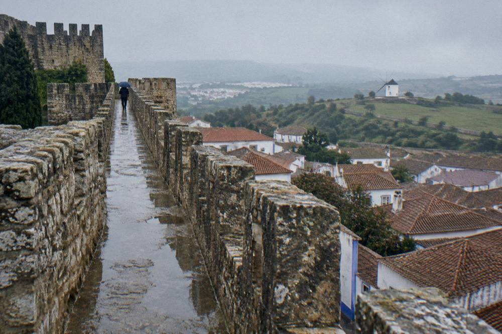 Stone town wall with crenellated walkway above red rooftops and countryside