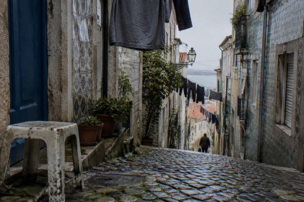 A narrow cobblestone alley in Lisbon's Alfama district lined with traditional tiled buildings and hanging laundry