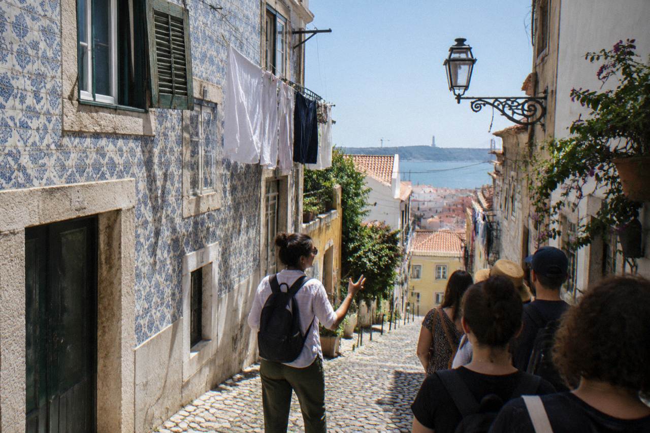 A guide leading a small group through a cobblestone street in Lisbon's Alfama district, with colorful buildings and a clear sky.