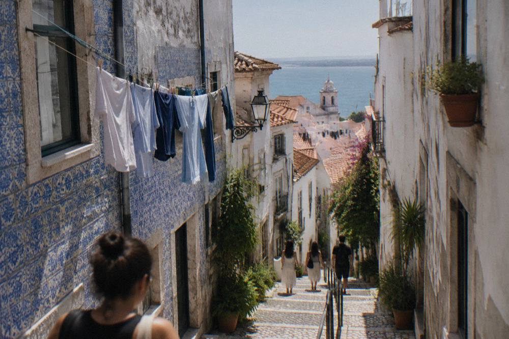 Crowded narrow alley in Alfama with tiled walls and steep steps