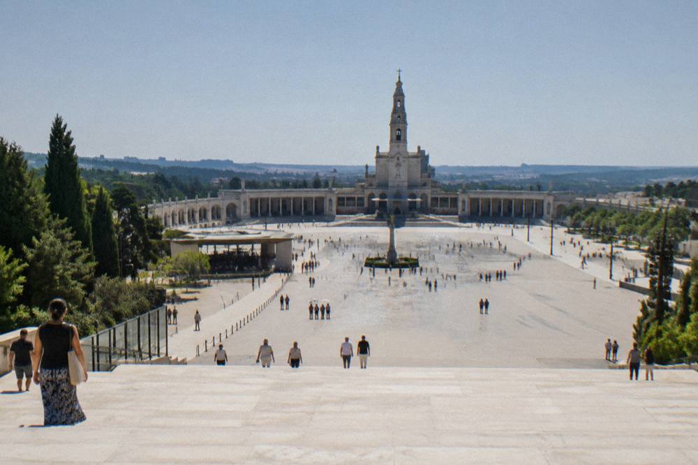 A wide esplanade in front of a basilica with a long colonnade and a smooth polished stone ground reflecting daylight