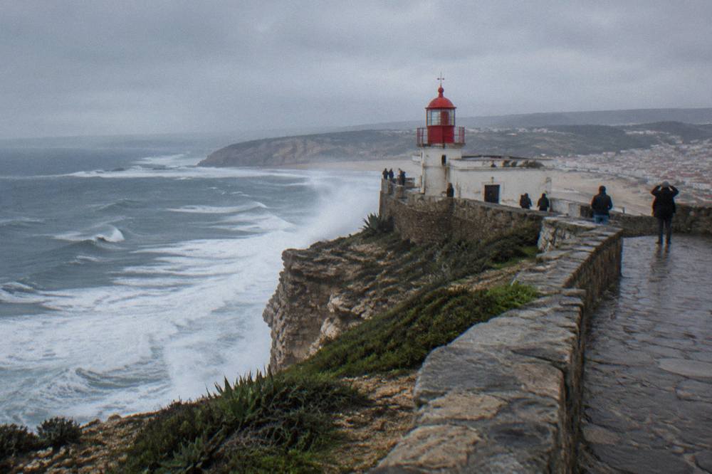 Clifftop lighthouse and viewpoint above the wide Atlantic beach at Nazare, with headland curving into the distance.