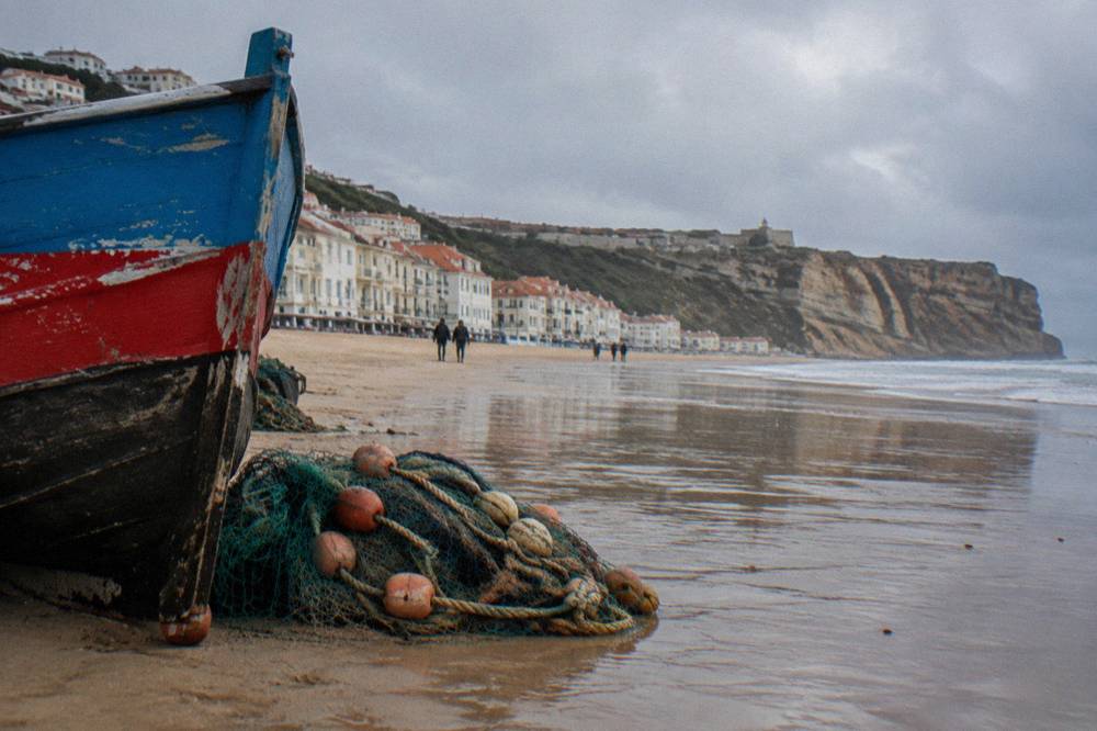 Fishing boats drawn up on the wide sandy beach at Nazare, with colourful sterns facing the restaurant row along the seafront.