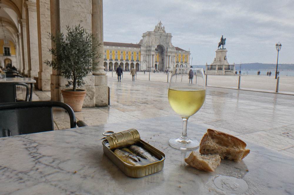 An open tin of sardines with bread and a glass of white wine on a marble counter