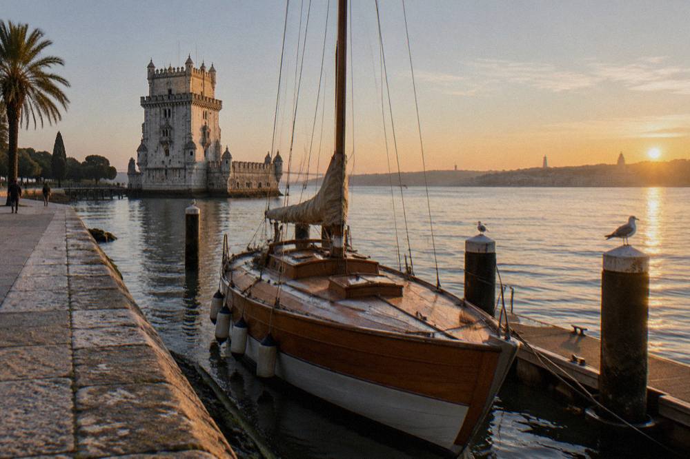 Wooden sailboat moored at a riverside dock with historic Lisbon buildings behind it