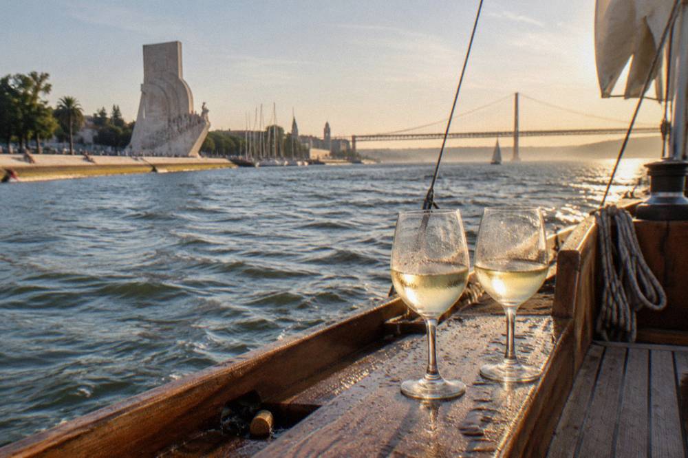Two glasses of white wine on a wooden boat deck with the river and bridge in the background