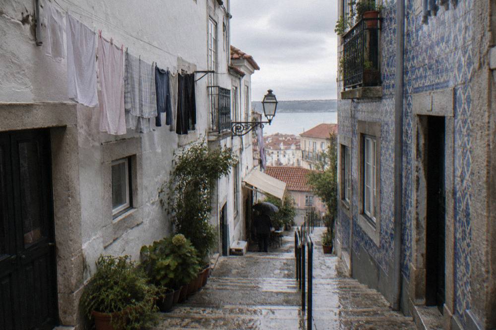 A narrow Mouraria street with small tascas and hanging laundry above the tables