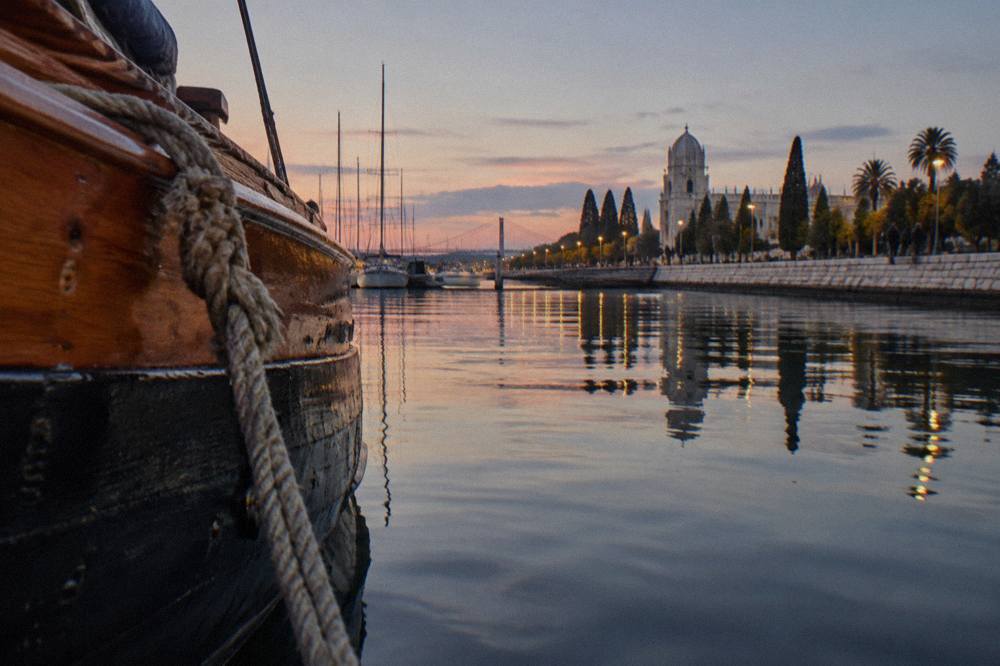 A traditional wooden boat moored on the Tagus at dusk with city lights reflecting on the water