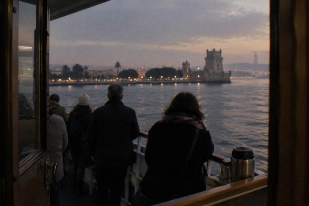 Passengers on a sailboat watching the city skyline glow above the Tagus river at dusk