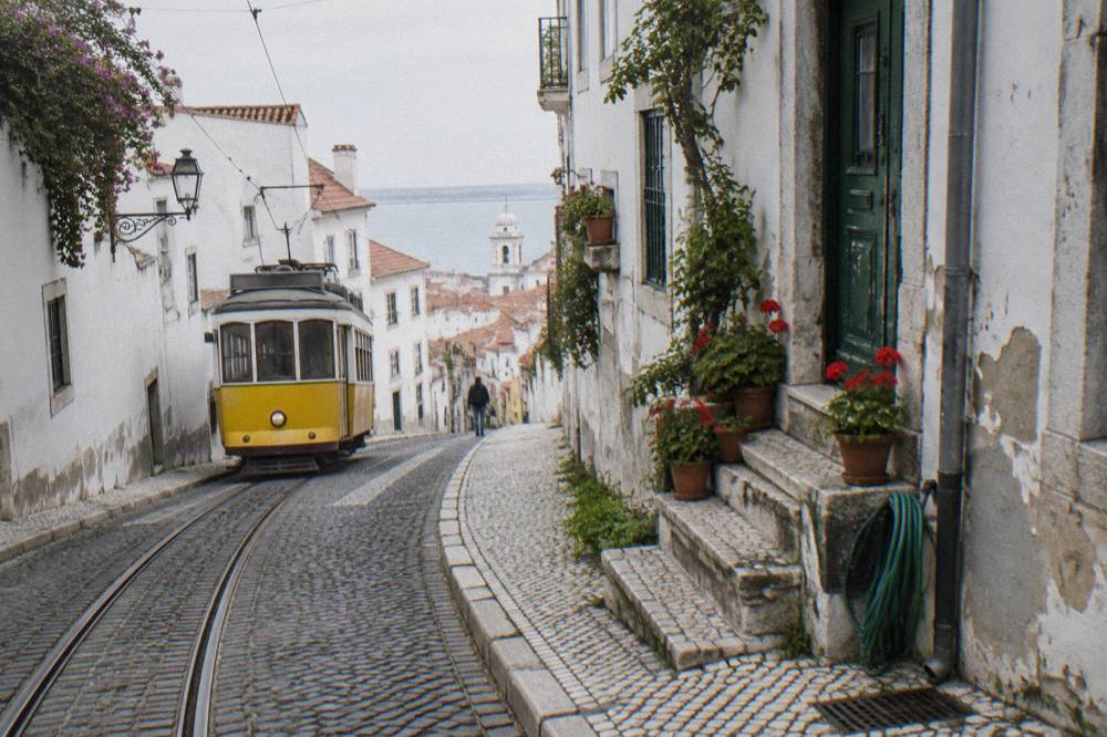 A narrow Alfama street with a yellow tram track curving between old buildings