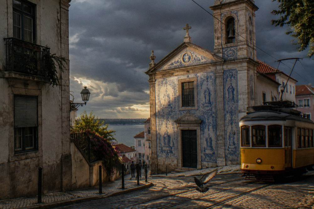 A vintage tram passing a tiled church facade on a Lisbon hill street