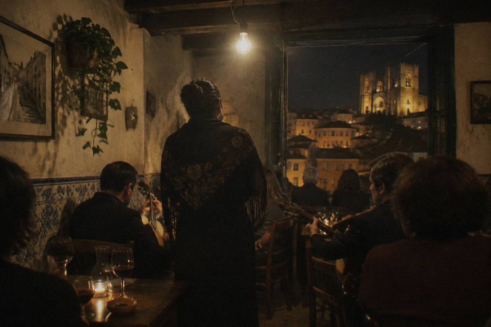 A dim tavern interior with a fado singer standing between crowded tables