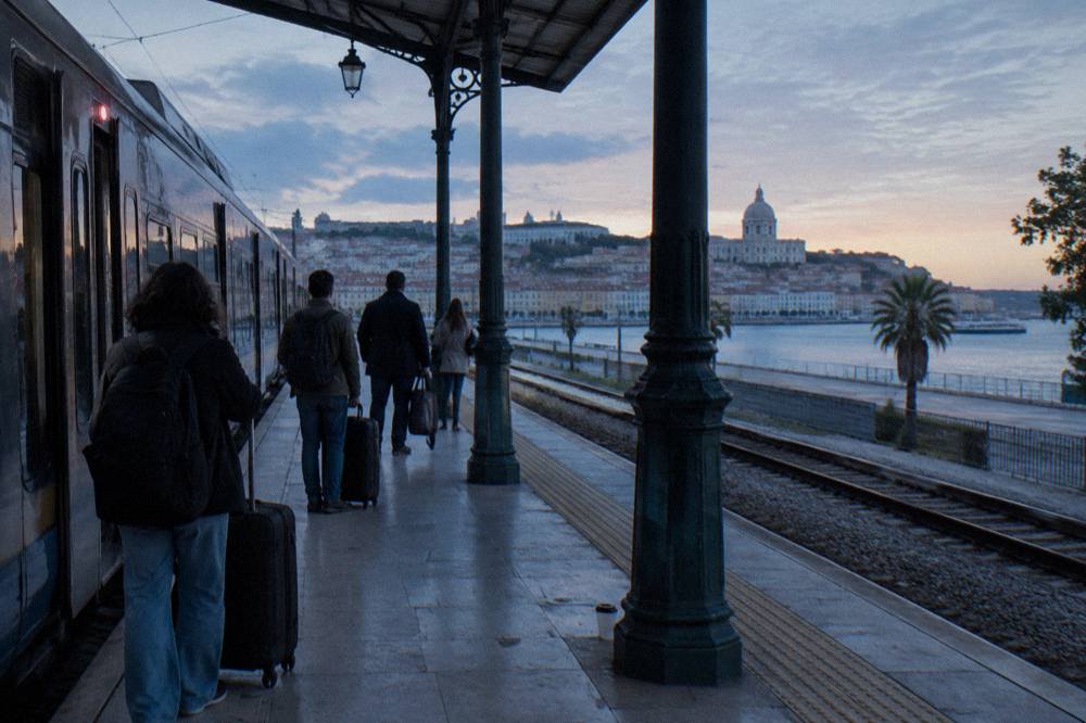 A long-distance train in dawn light at Santa Apolonia station in Lisbon, passengers with cases along the platform edge