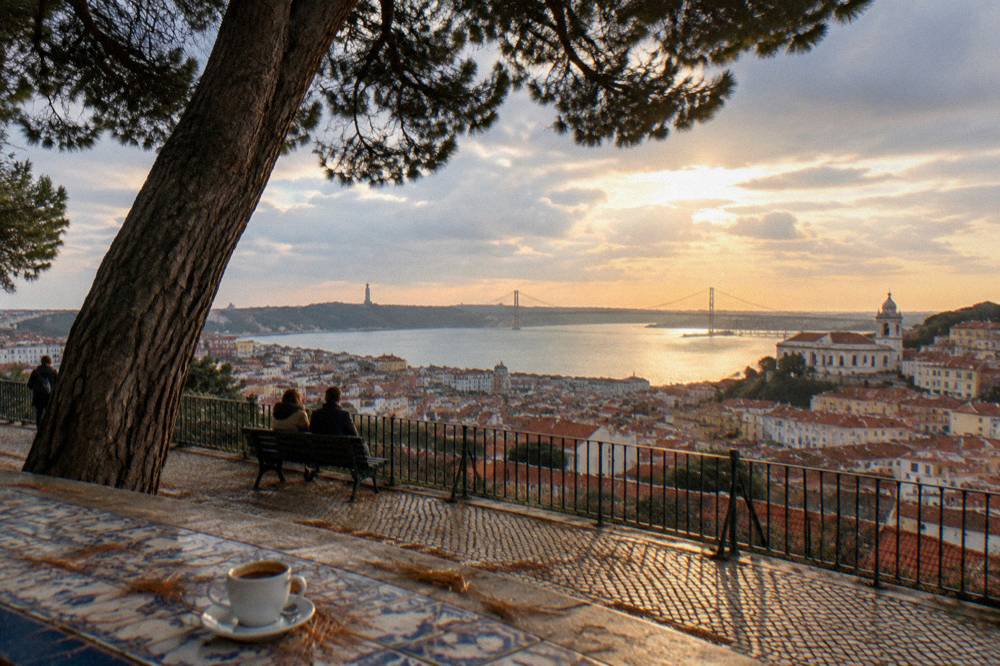 View over Lisbon rooftops and the river from a hilltop terrace in late afternoon light