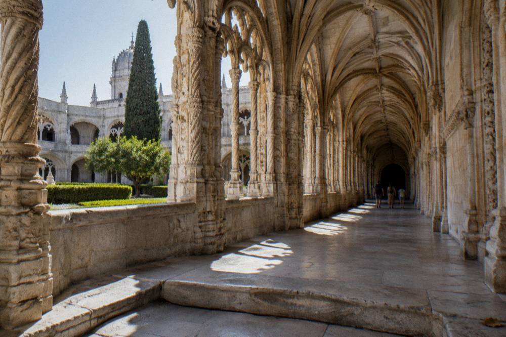Ornate stone cloister arcade of Jeronimos Monastery under a bright sky