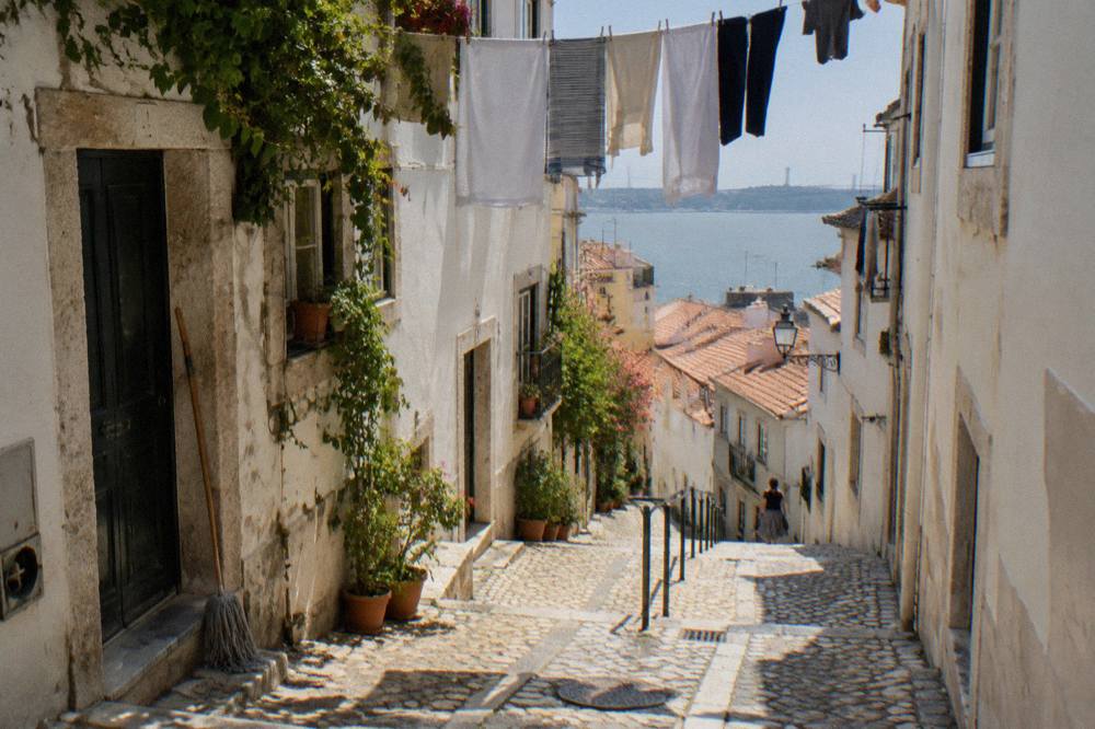Cobbled Alfama lane climbing between whitewashed houses with laundry overhead
