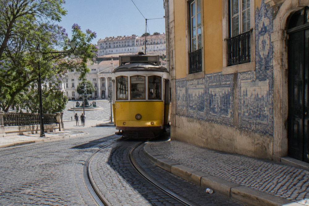 Yellow classic tram rounding a corner past tiled facades in a Lisbon street