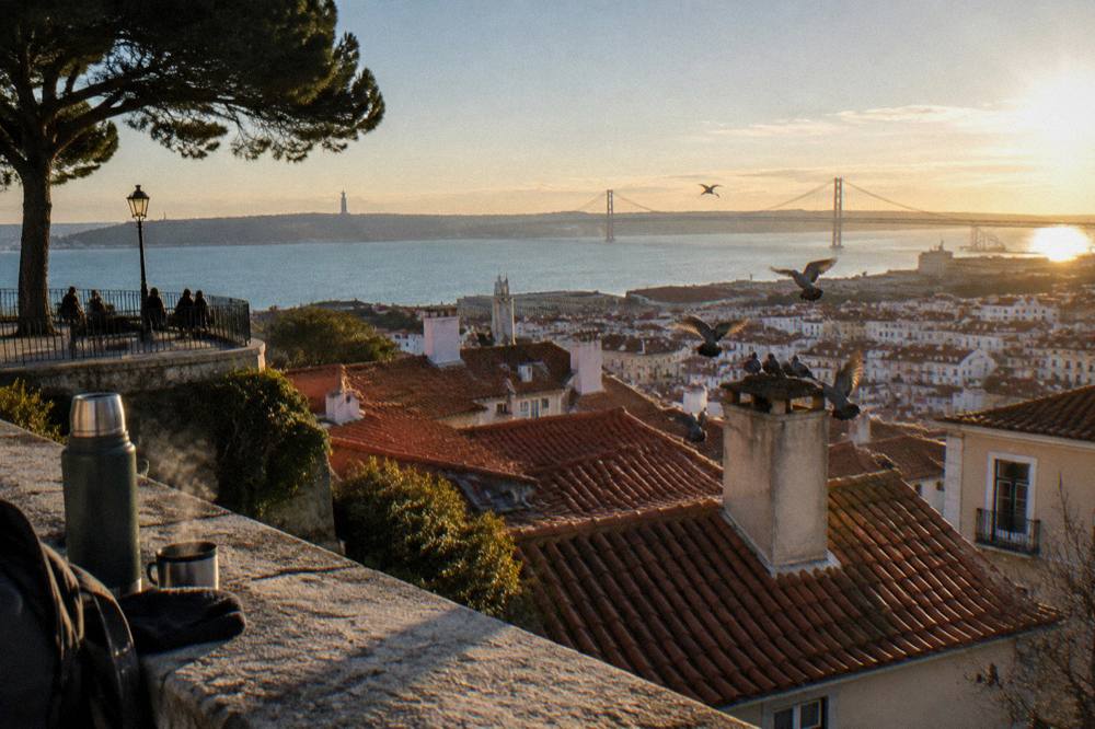 Wide cityscape of Lisbon rooftops descending to the Tagus river at golden light
