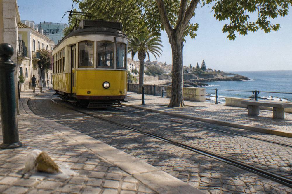 Yellow vintage tram on a tree-lined street in Cascais near the seafront