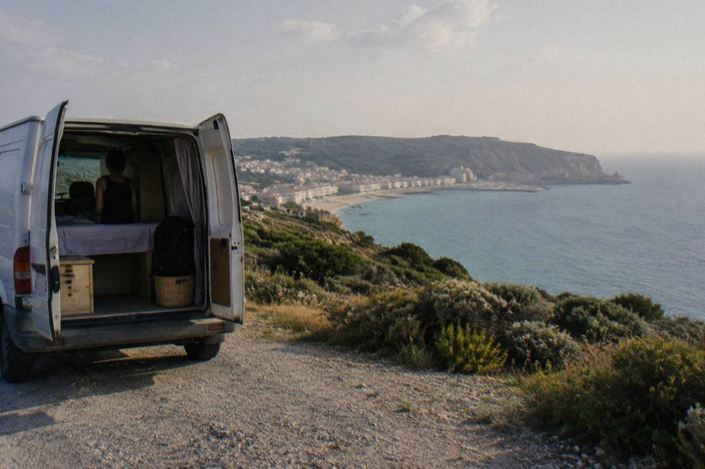 Small tour van parked on a coastal road above a beach town south of Lisbon