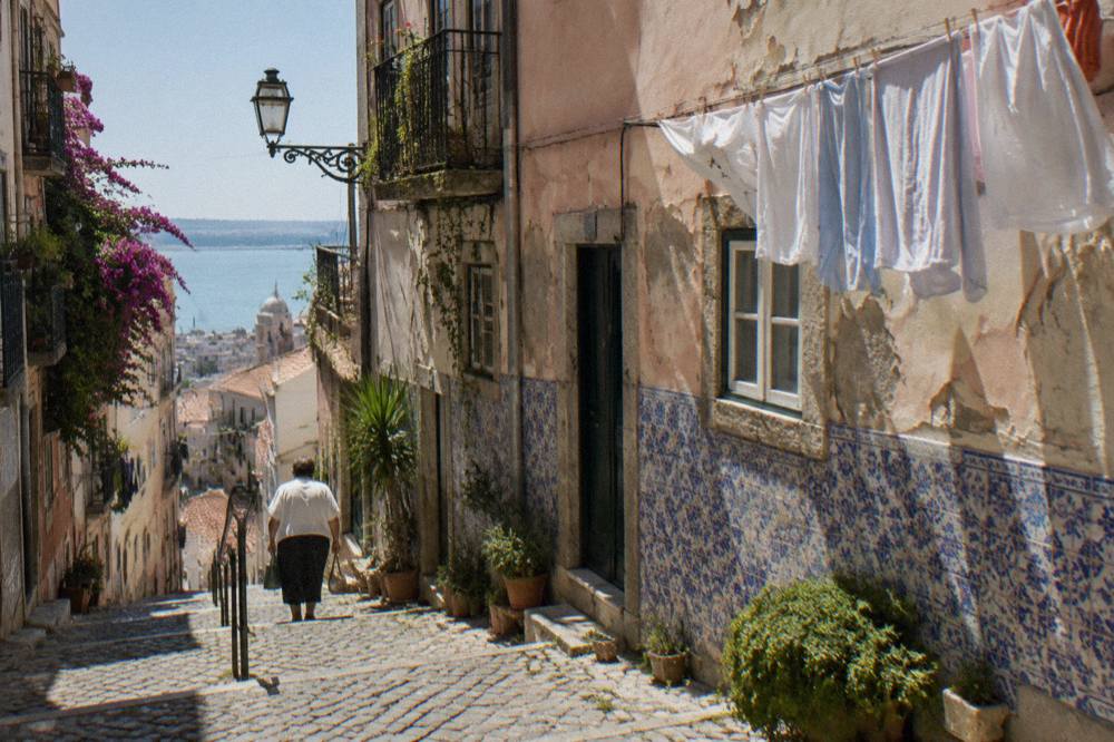 Narrow stepped street in Alfama with pastel-coloured buildings and laundry overhead