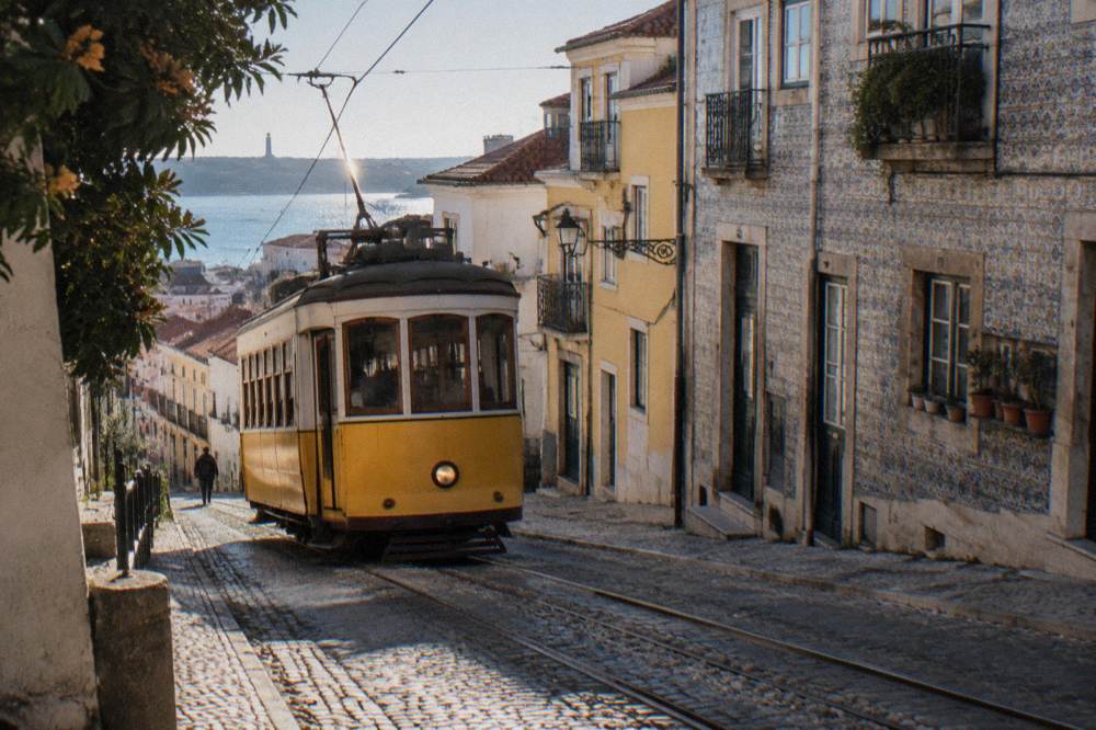 Yellow historic tram on a Lisbon street with hills and buildings behind