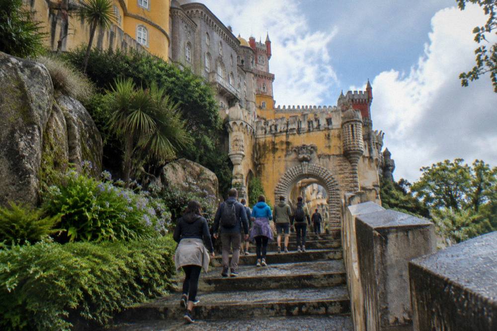 A small group of visitors walking up a stone path toward the Pena Palace gate in the morning