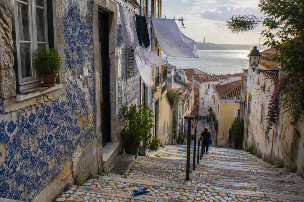 Narrow tiled street in Alfama with laundry overhead and a view to the river