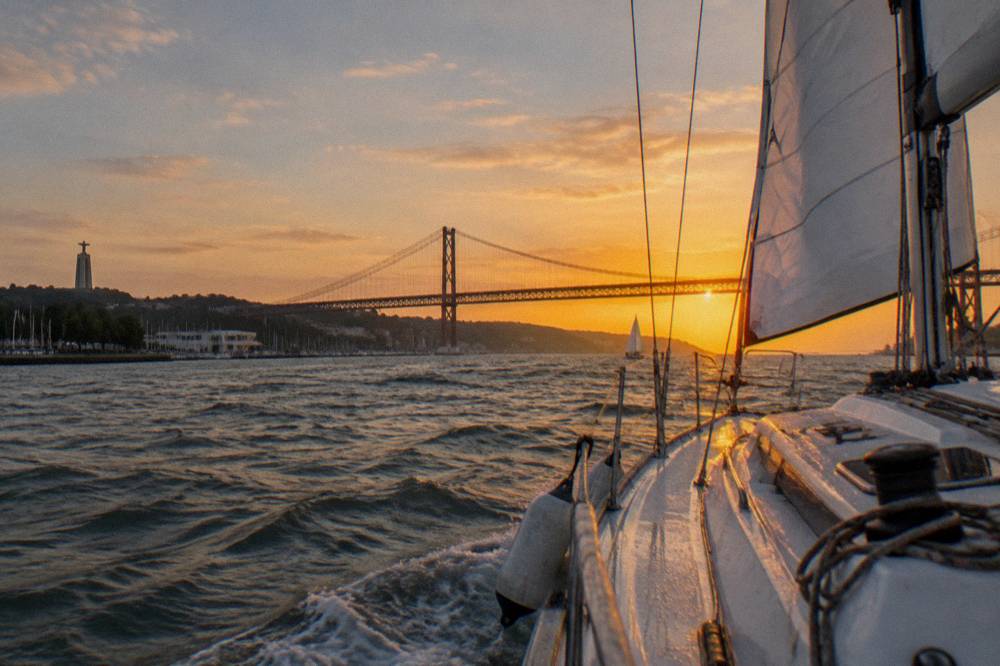 Sailboat on the Tagus river passing the 25 de Abril bridge at golden hour