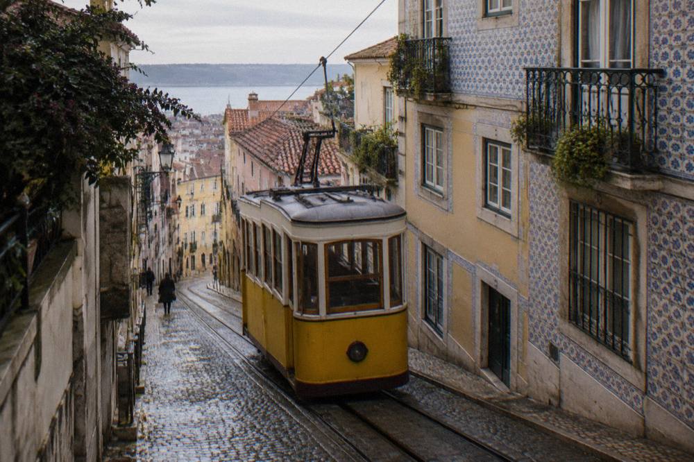 Vintage tram climbing a steep narrow street between pastel tiled buildings in Lisbon