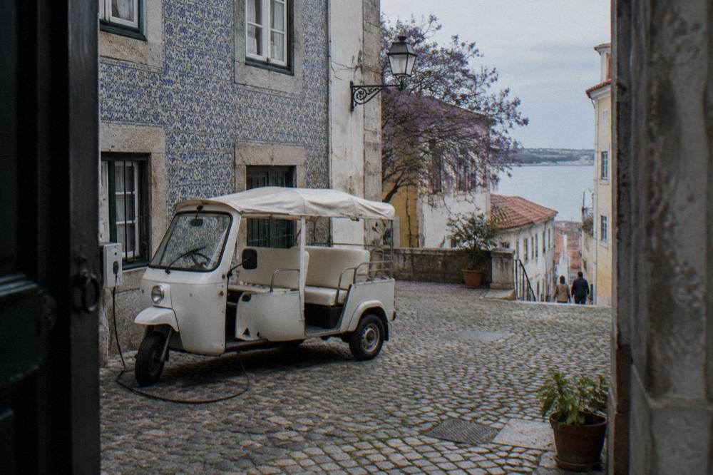 Electric tuk tuk vehicle parked on a cobbled street beside tiled buildings in old Lisbon