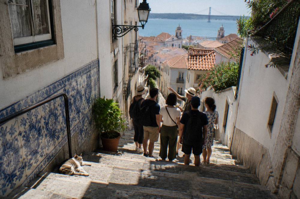 A guide speaking to a small cluster of visitors on a narrow tiled Alfama staircase